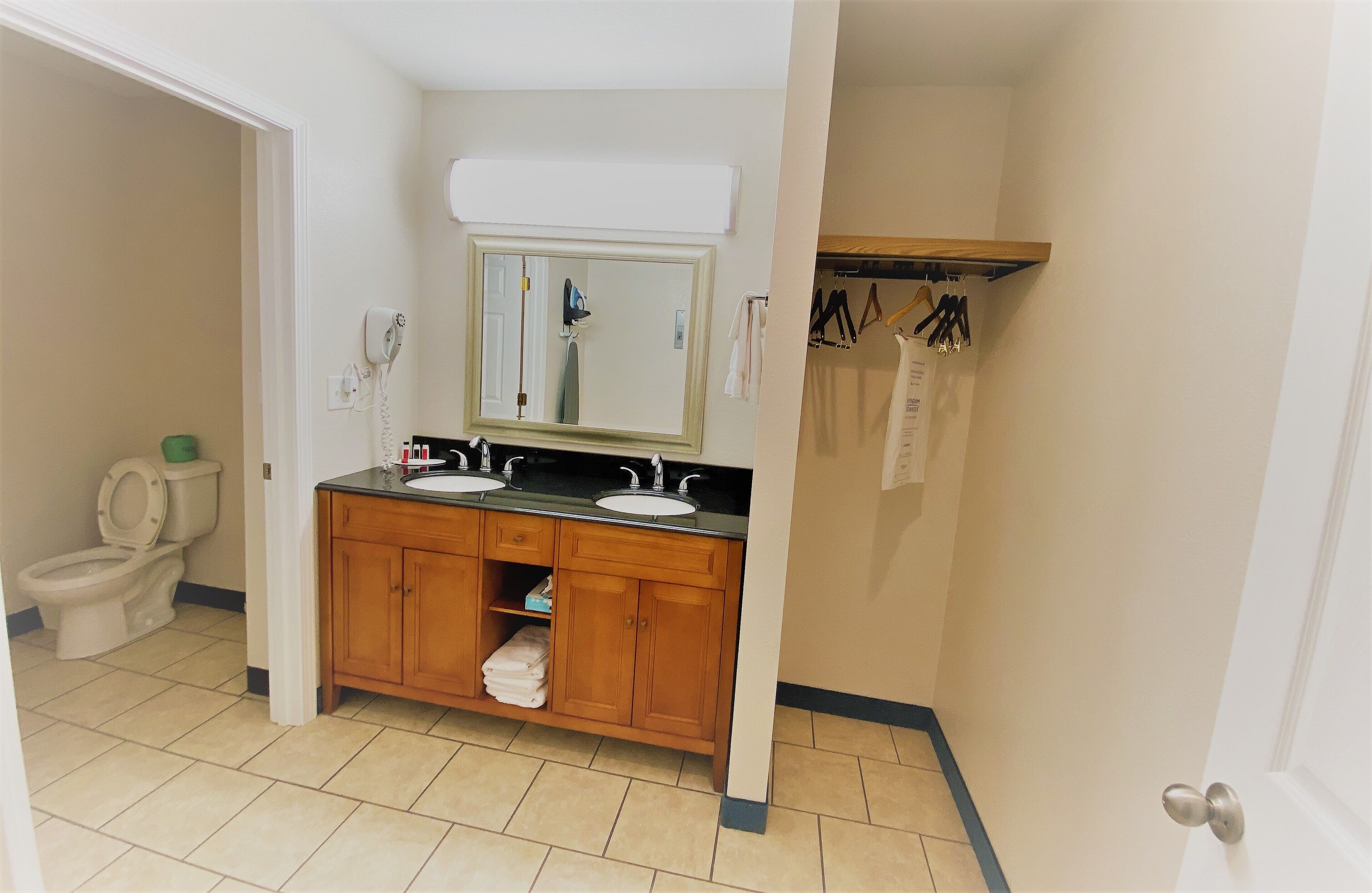 Een badkamer met een houten wastafelmeubel, twee wastafels, een spiegel en een toilet.