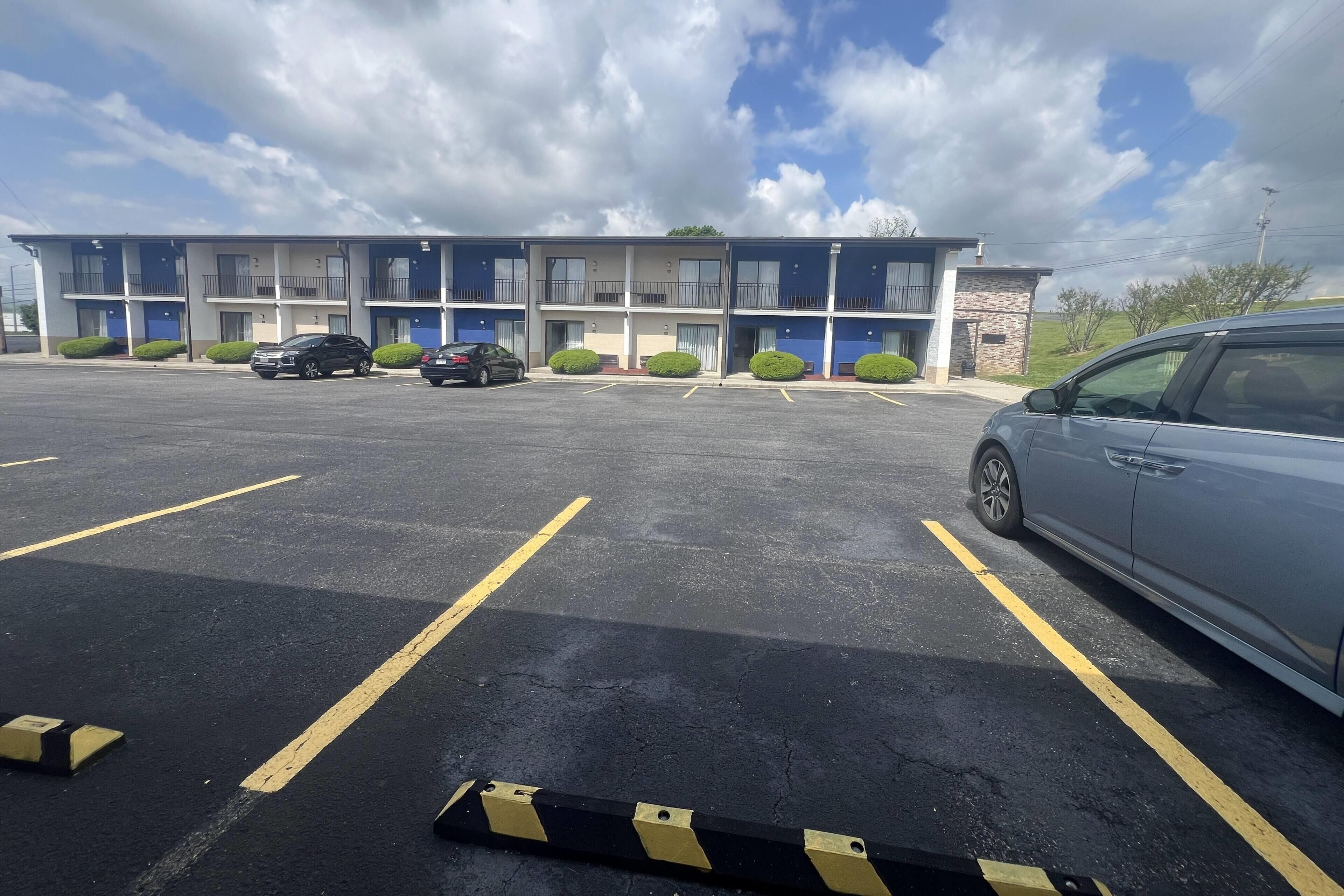 A multi-story motel with a parking lot, several cars, and a clear sky.