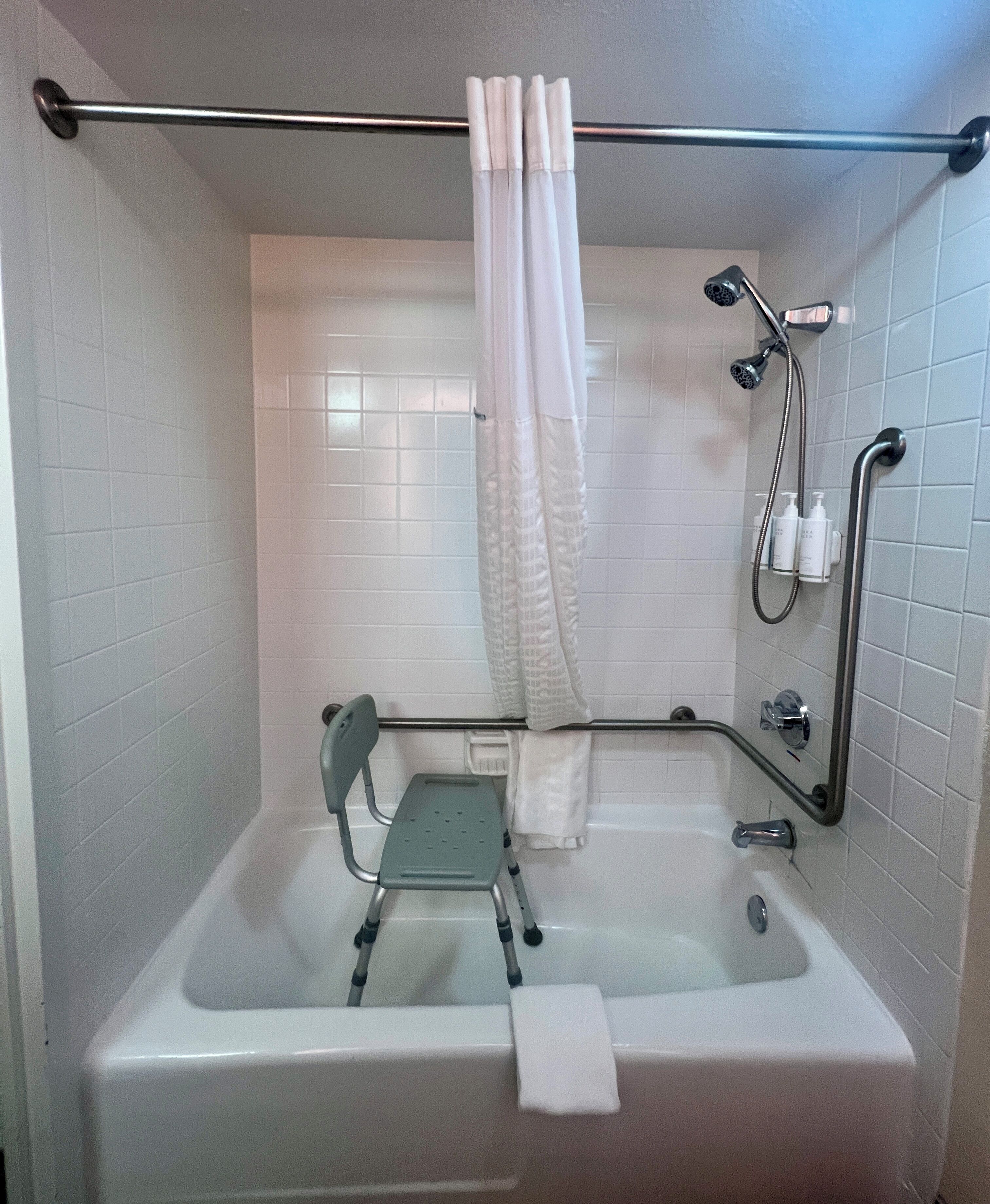 A bathroom with a bathtub, shower, grab bar, and a wheelchair-accessible bench.