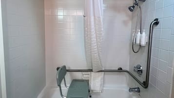 A bathroom with a bathtub, shower, grab bar, and a wheelchair-accessible bench.