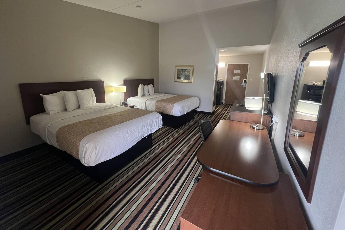 A hotel room with two beds, a desk, a mirror, and a door leading to a bathroom.