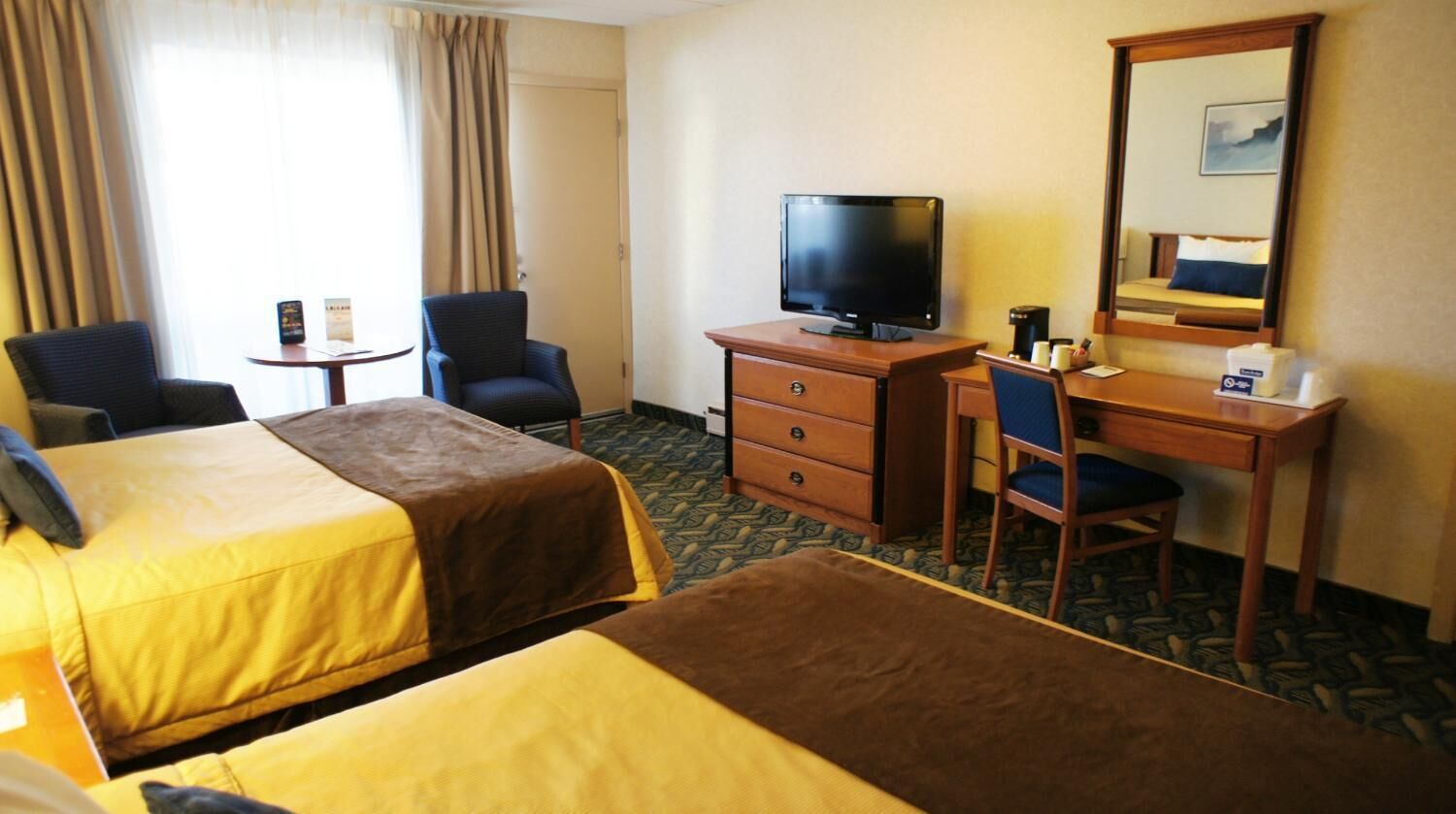 Hotelkamer met twee bedden, een bureau met televisie, een stoel, een tafeltje met een boek en een kopje, en een raam met gordijnen.