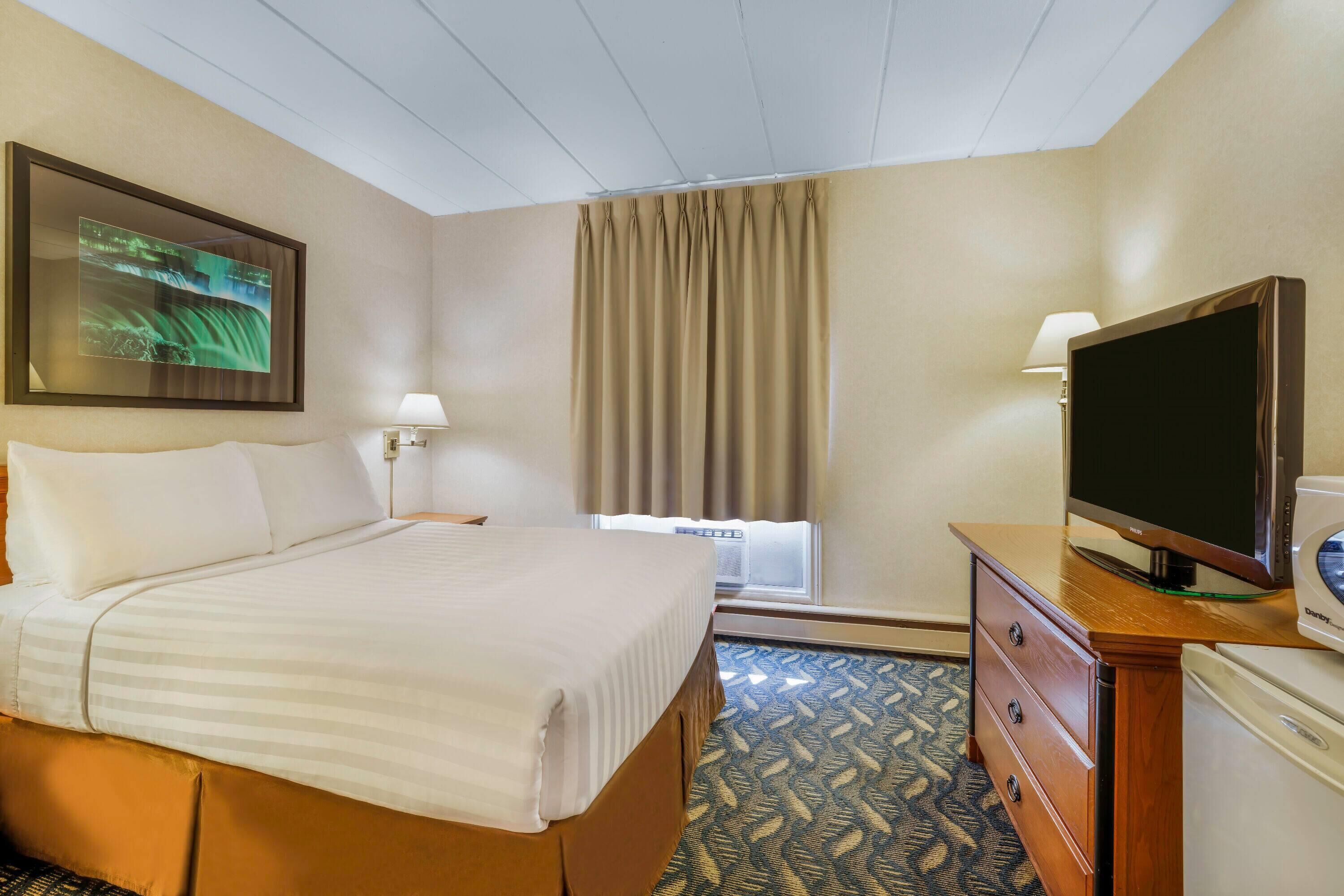 Una habitación de hotel con cama, televisión, escritorio con lámpara y ventana con cortinas.