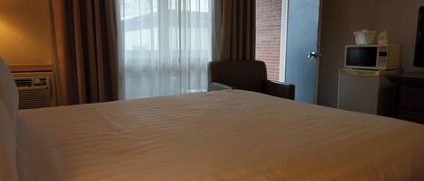 Ein Hotelzimmer mit einem großen Bett, einem Sessel, einem Fernseher und einer Mikrowelle auf einem kleinen Tisch.