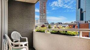 Un balcón con sillas blancas, un muro de ladrillo y una jardinera con flores.