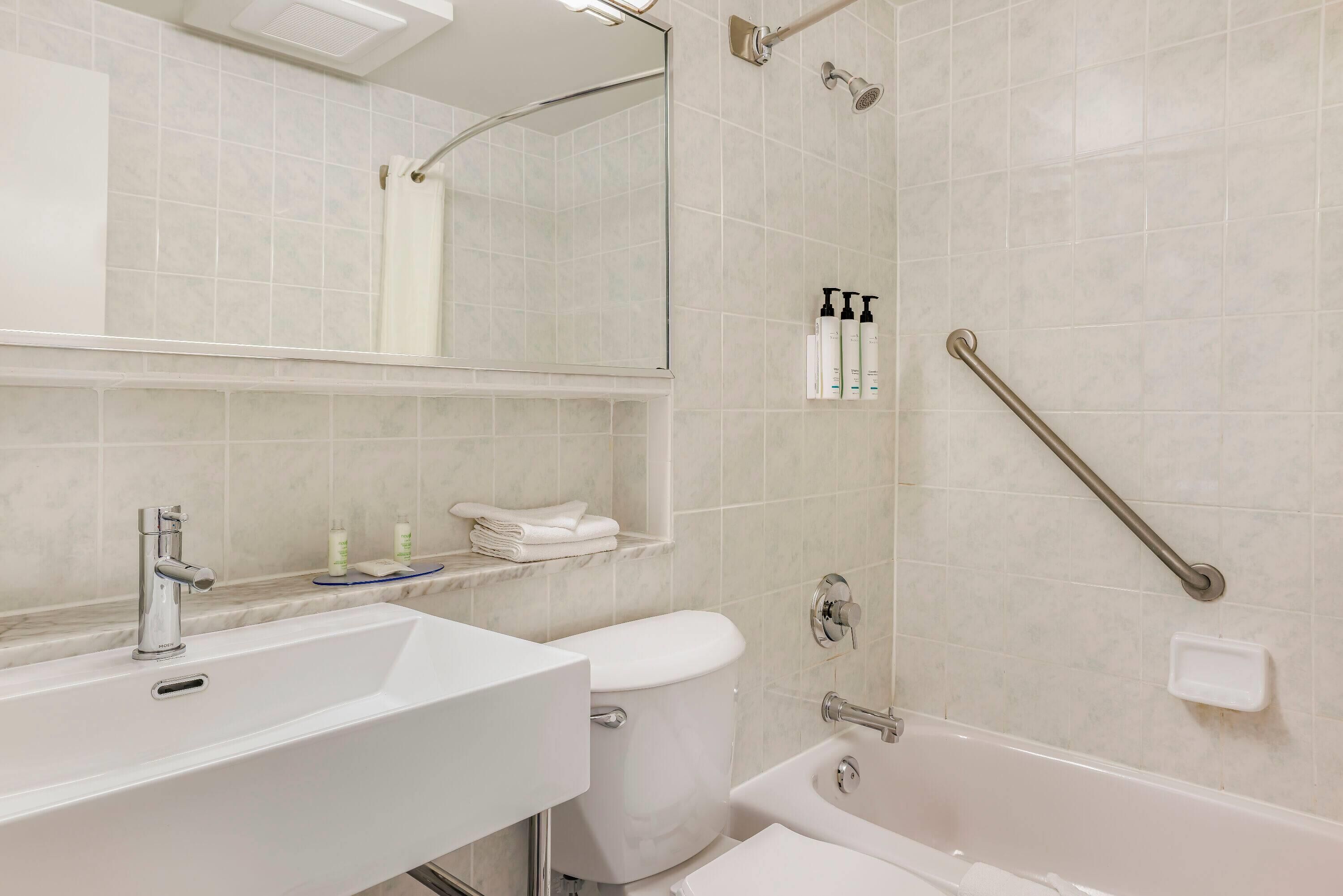 A bathroom with a white sink, toilet, and bathtub. There is a showerhead and a handrail on the wall.
