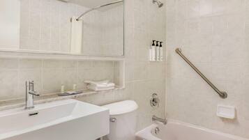 A bathroom with a white sink, toilet, and bathtub. There is a showerhead and a handrail on the wall.