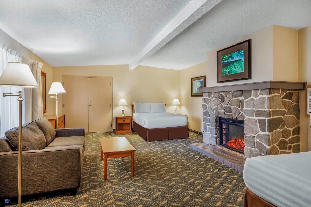 Una habitación de hotel con una cama, un sofá, una mesita, una chimenea y un televisor sobre la chimenea.