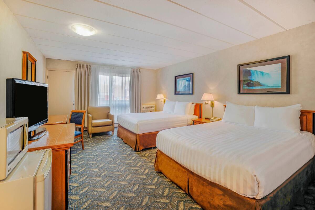 Habitación de hotel con dos camas, un escritorio, televisor, una silla y un cuadro en la pared.