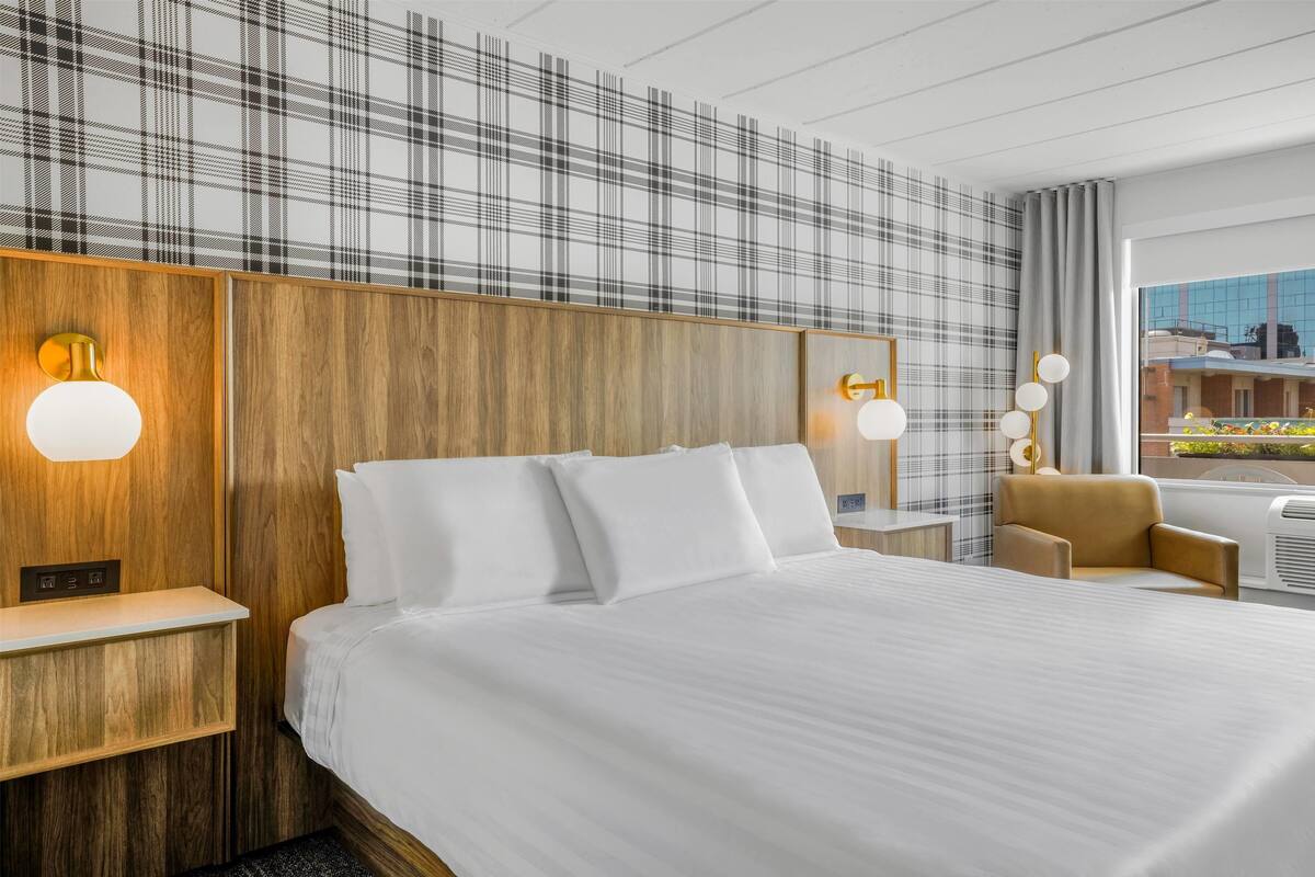 Habitación de hotel con una cama grande, cabecera de madera, tocador con espejo y vista a un edificio por la ventana.