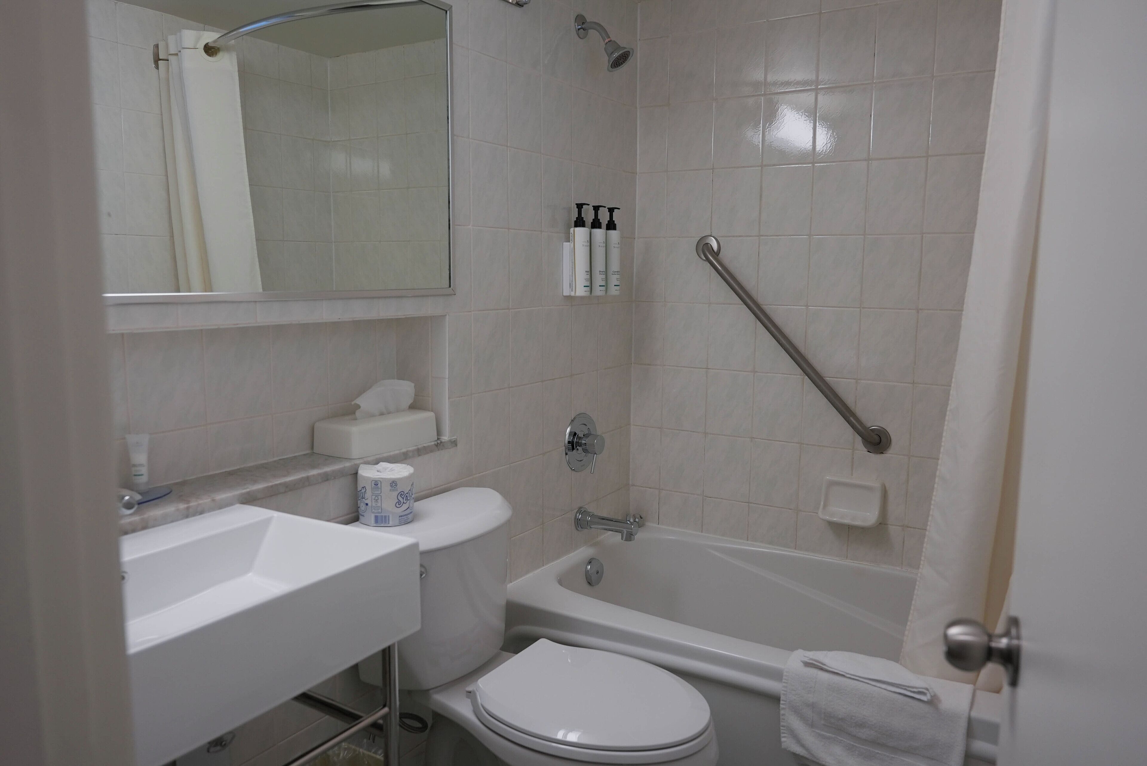 A bathroom with a white sink, toilet, and bathtub. There is a showerhead and a grab bar installed.