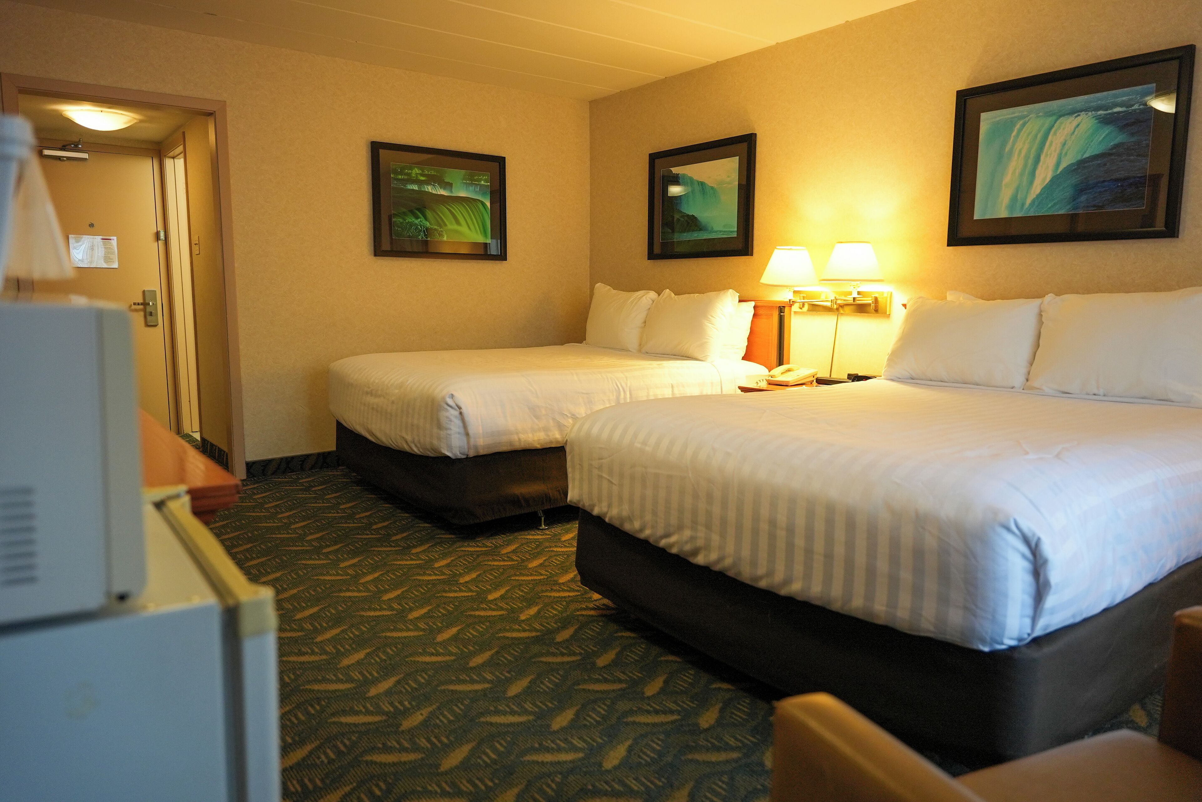 A hotel room with two beds, a desk, and a lamp.