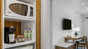 Habitación de hotel con microondas, cafetera, refrigerador y un pequeño escritorio con una silla.