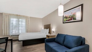 Une chambre d’hôtel avec un lit, un canapé bleu, un bureau et une fenêtre avec des rideaux.