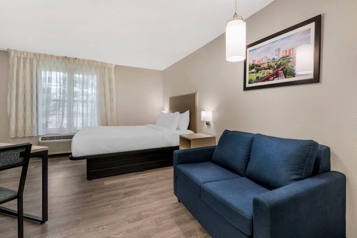 Une chambre d’hôtel avec un lit, un canapé bleu, un bureau et une fenêtre avec des rideaux.