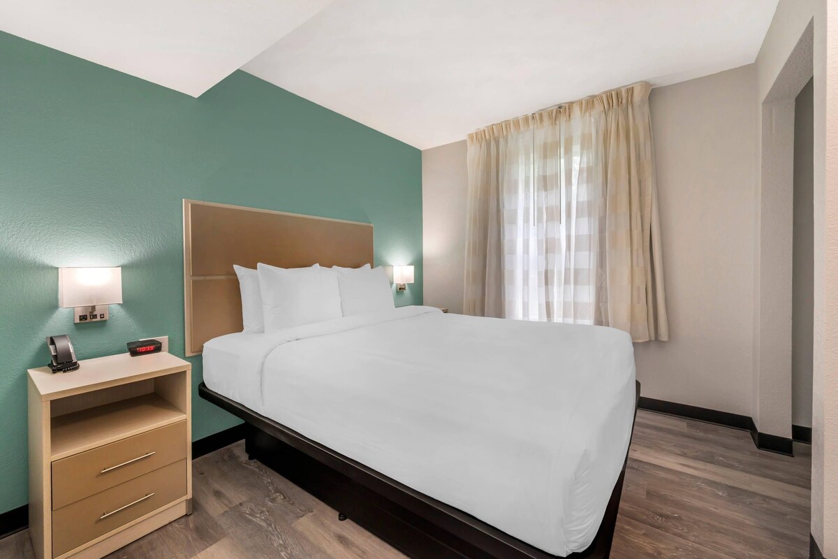 A hotel room with a bed, a nightstand with a lamp, and a window with curtains.