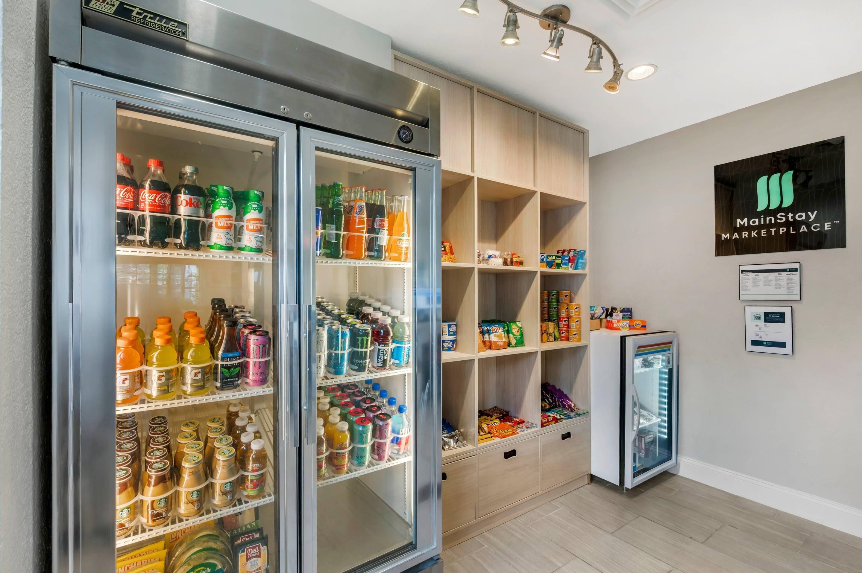 Ein MainStay Marketplace mit zwei großen Kühlschränken, gefüllt mit Getränken und Snacks, sowie einem kleineren Kühlschrank.