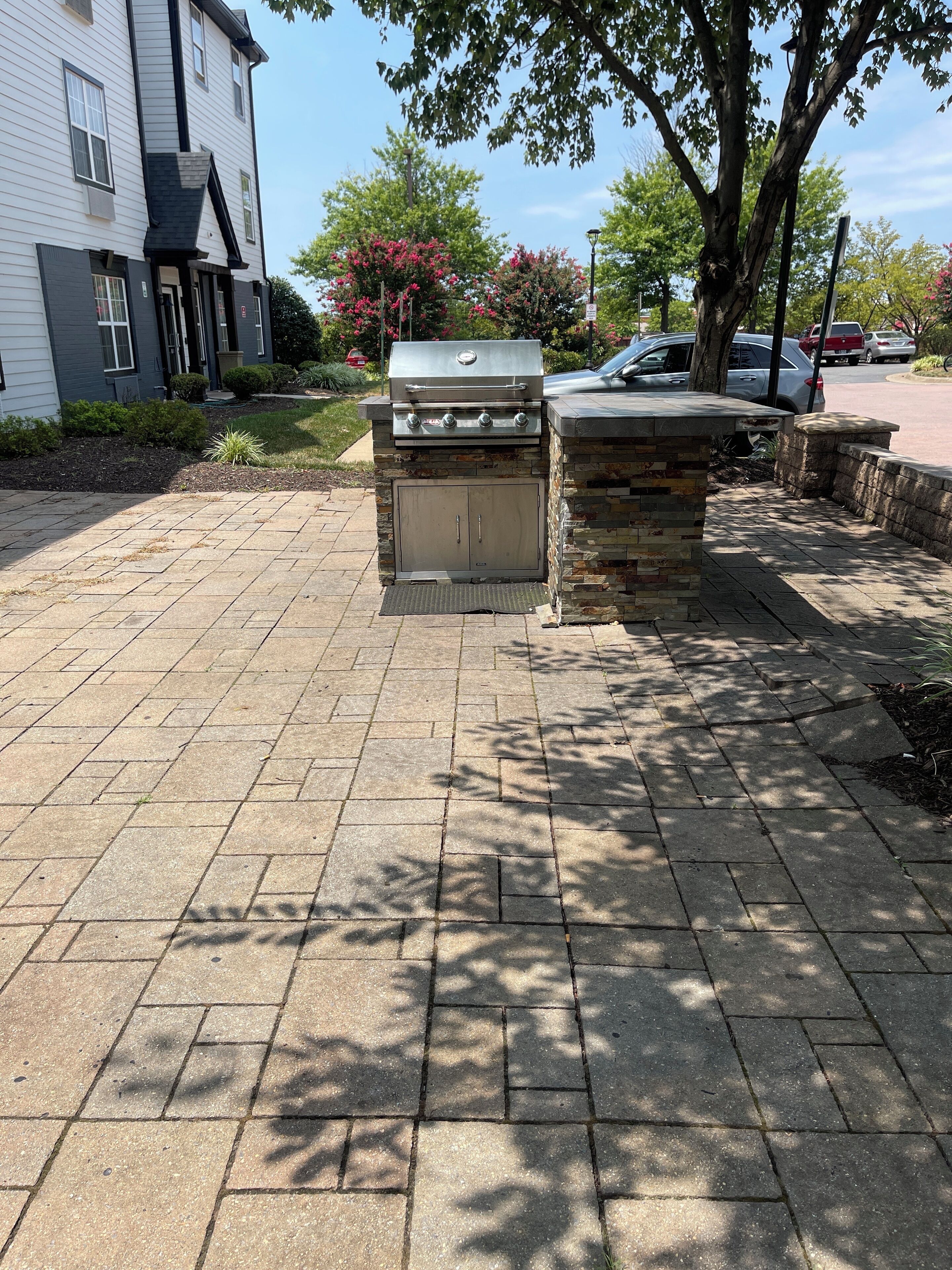A barbecue grill and stone structure in a residential area with a paved walkway.