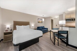 Ein Hotelzimmer mit Bett, Nachttischen, Schreibtisch mit Stuhl, Sofa und einer Küchenzeile.