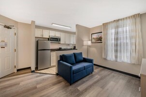 Un espacio habitable compacto con kitchenette, un sofá y una ventana con cortinas traslúcidas.