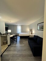 Habitación de hotel con cama, escritorio, silla, sofá, televisor y un cuadro en la pared.