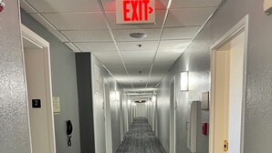 Een hotelgang met een vluchtwegbord, deuren met de nummers 2 en 3, en een telefoon aan de muur.