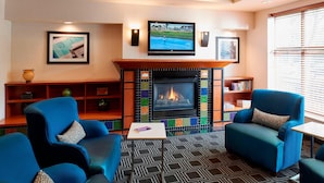 Una sala de estar moderna con chimenea, sillones azules, una mesa de centro y un televisor montado sobre la chimenea.