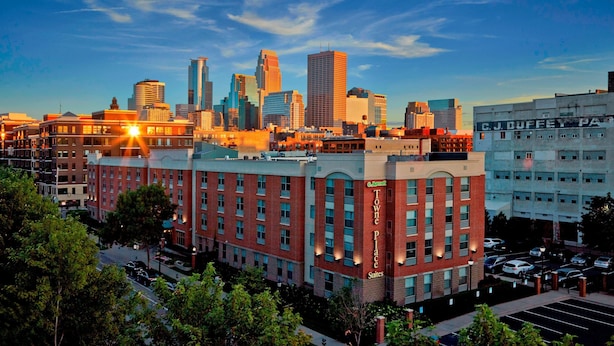 Un hotel con un letrero destacado de "Towne Place Suites" y una vista del horizonte de la ciudad al fondo.