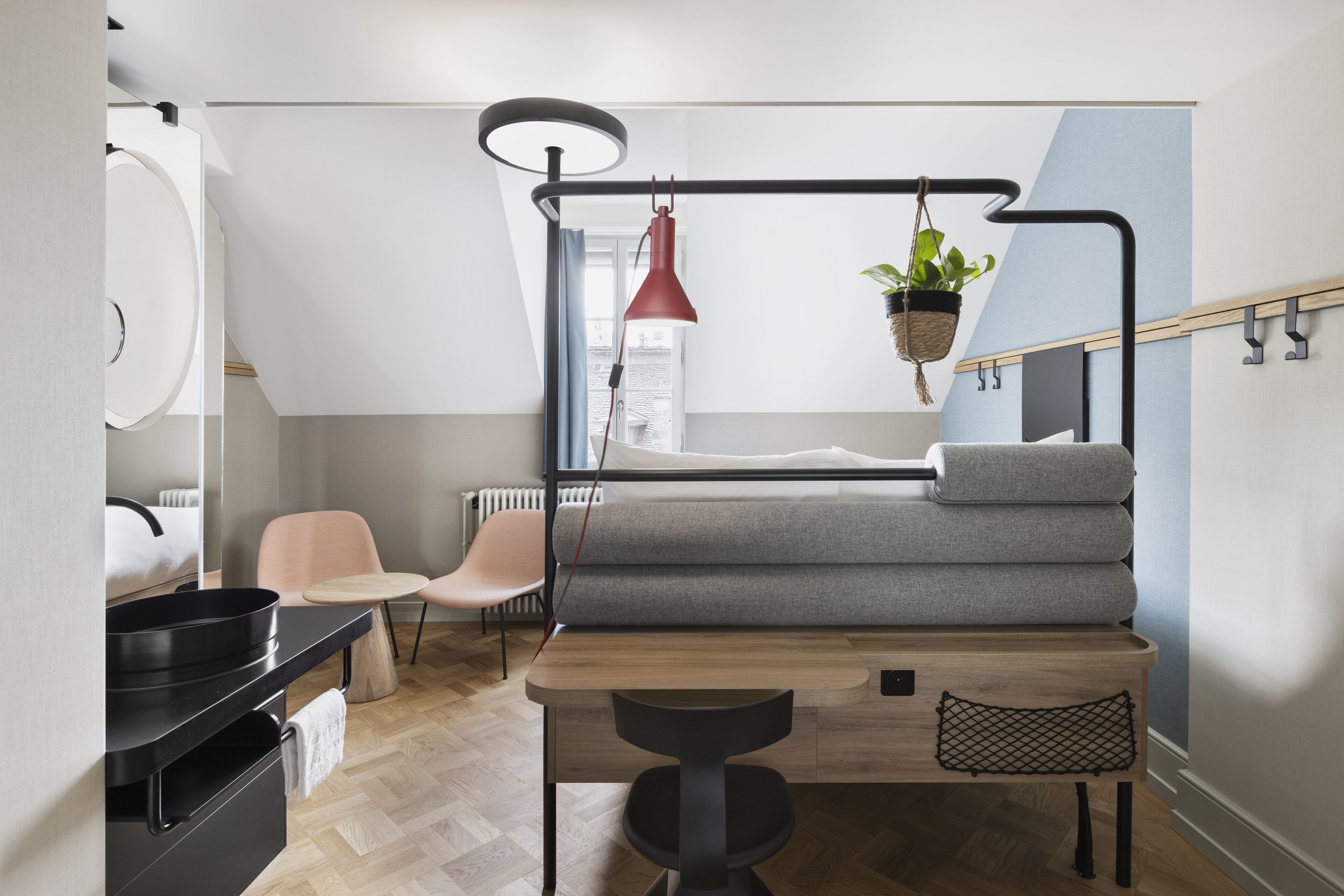 A compact, modern bedroom with a loft bed, a small table, a chair, and a hanging plant.