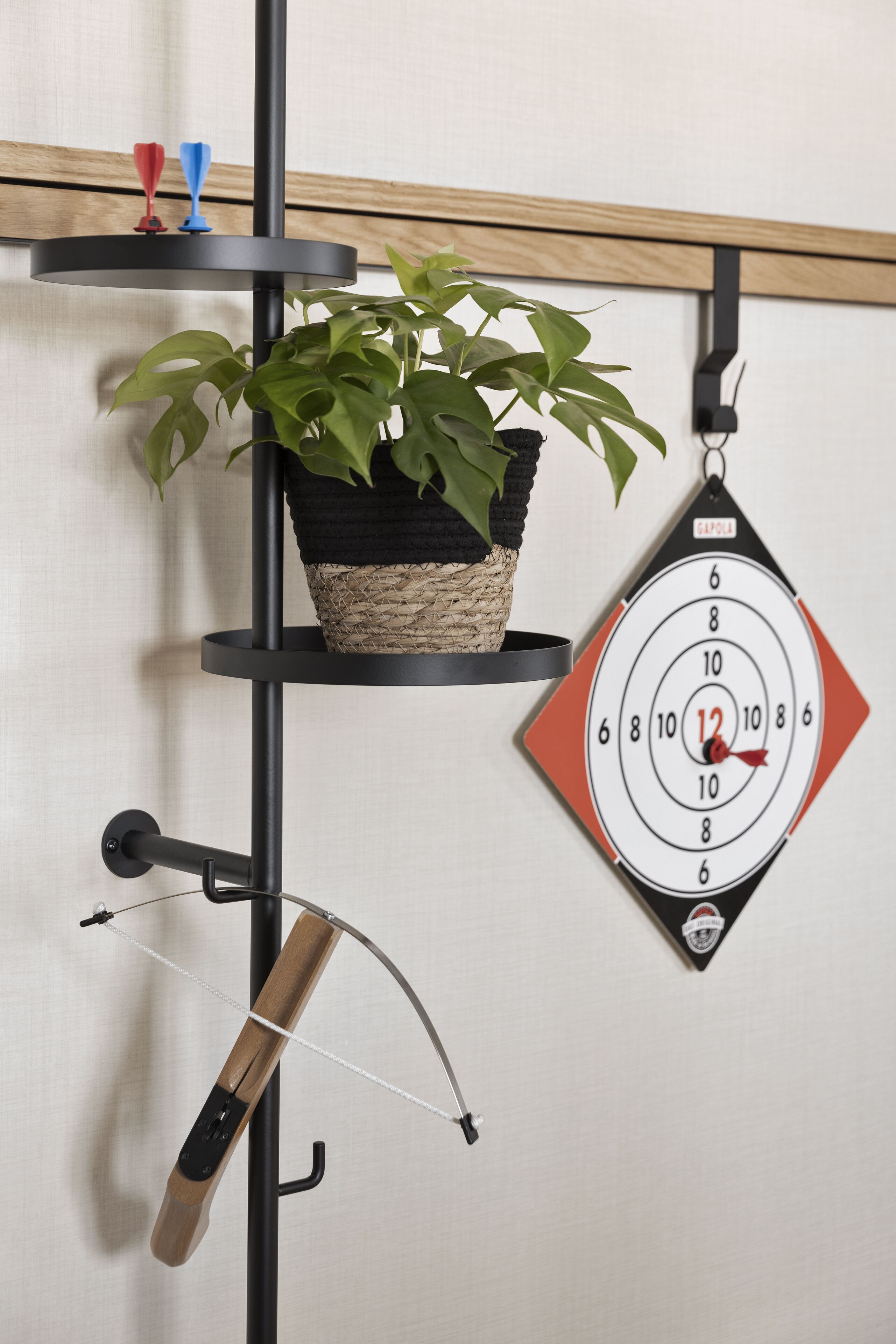 A wall-mounted shelf with a potted plant, a dartboard, and a violin hanging on a black metal stand.