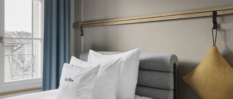 Quarto de hotel com uma cama, uma janela com cortinas azuis e vista para edifícios.