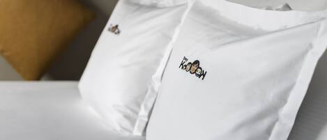 A bed with white pillows, one of which has a logo and text.