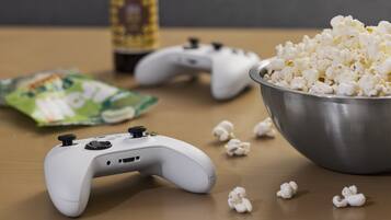 Un controller per videogiochi, una ciotola di popcorn e un pacchetto di snack su un tavolo di legno.