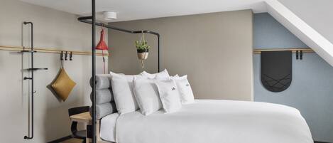 Un dormitorio moderno con una cama, una planta colgante, una lámpara colgante roja y suelo de madera.