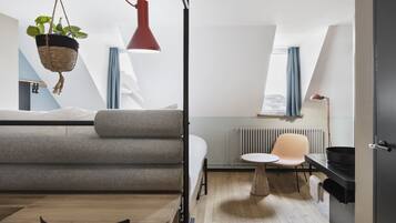 Habitación moderna y compacta con cama, una mesita, una silla, una planta colgante y una lámpara colgante roja.