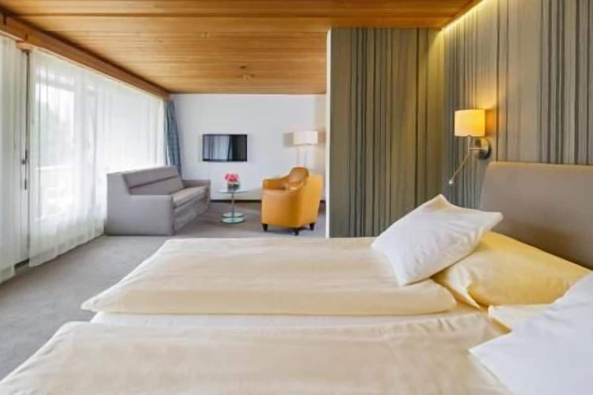 A hotel room with a bed, a sofa, a chair, a lamp, and a small table.