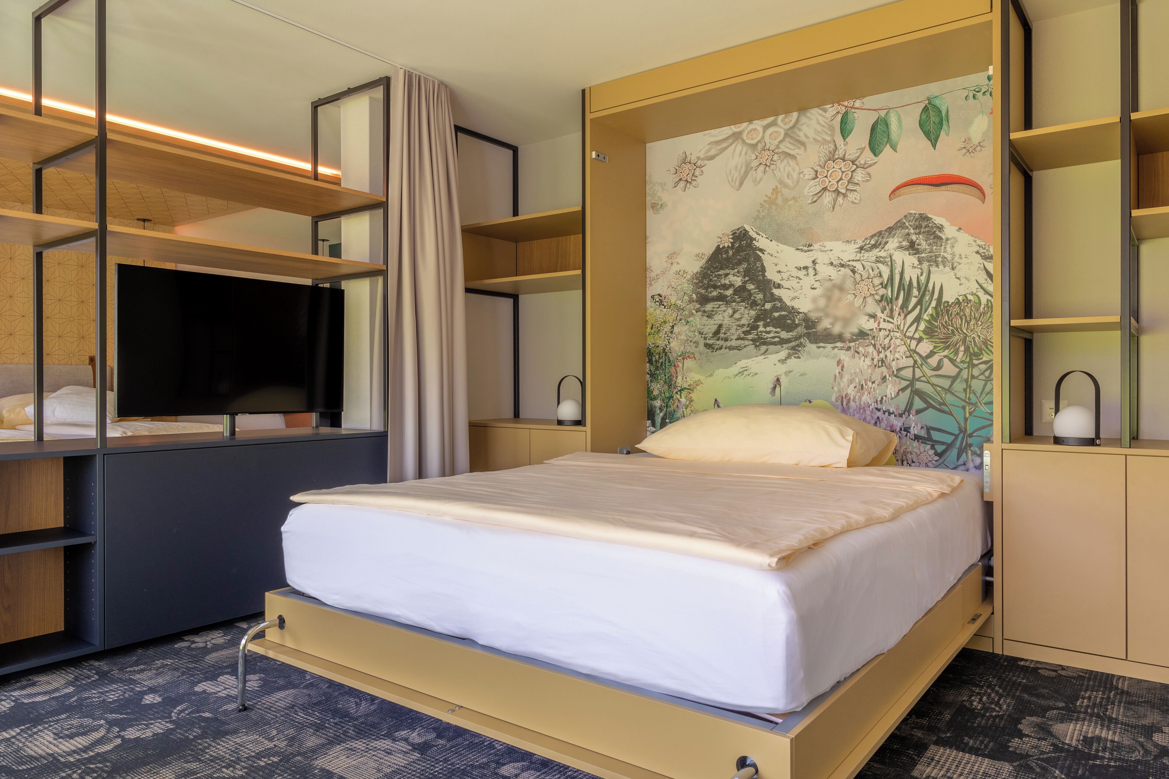 Habitación de hotel con una cama, televisor, un cuadro en la pared y estanterías empotradas.