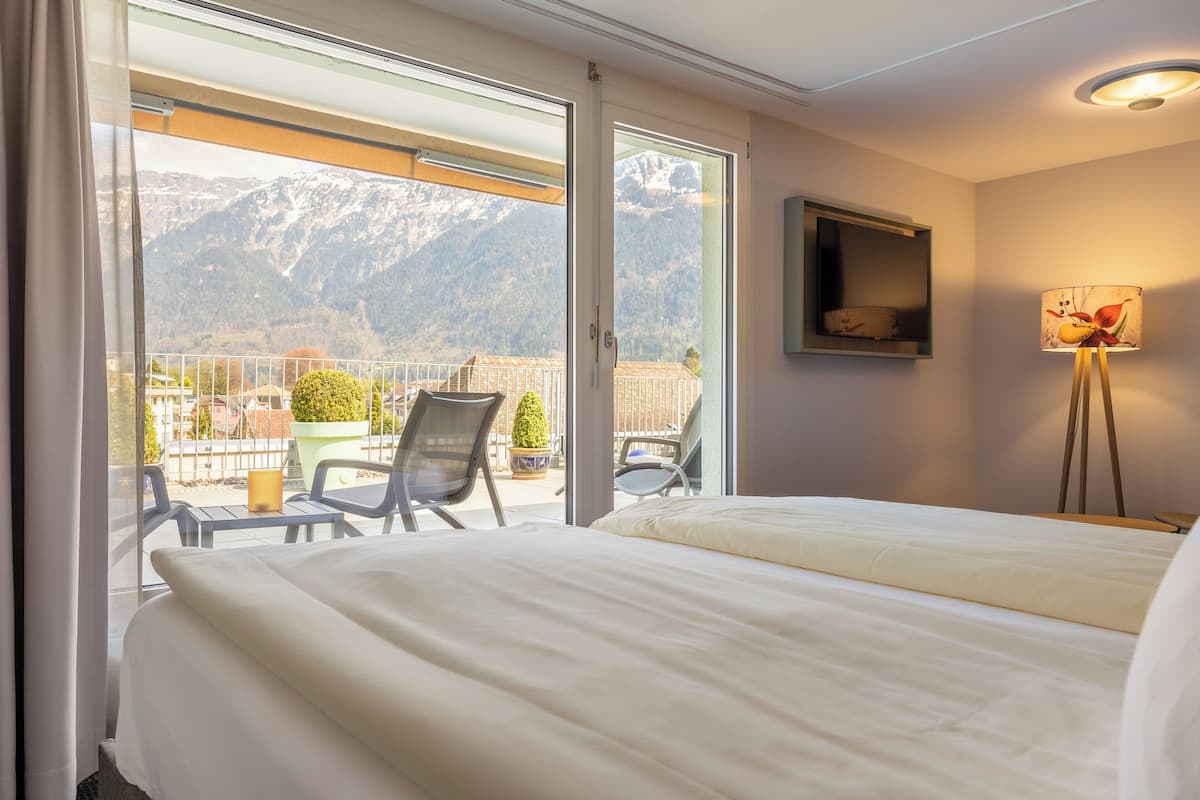 A hotel room with a bed, a chair, a table, a lamp, and a view of mountains through a sliding door.