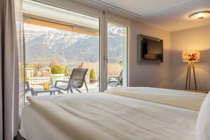 Habitación de hotel con cama, una silla, una mesa, una lámpara y vistas a las montañas a través de un ventanal corredera.