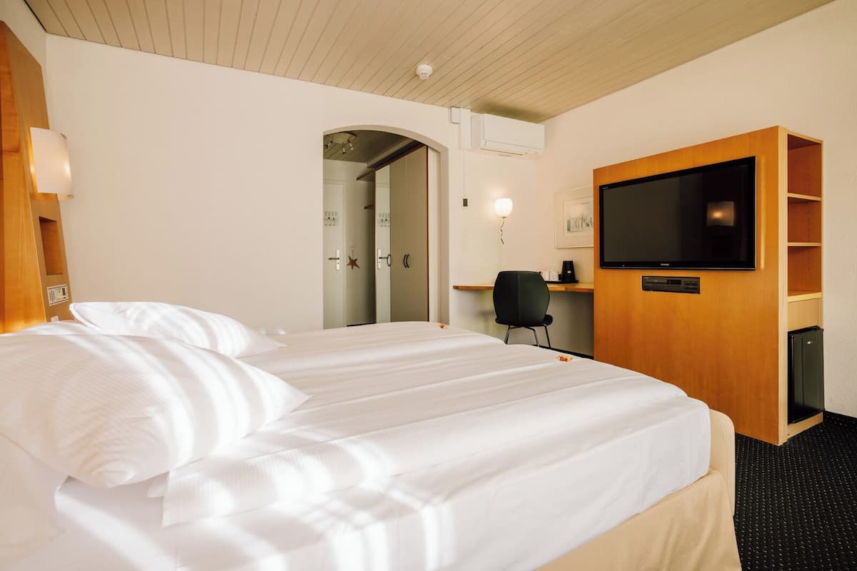 A hotel room with a large bed, a television, a desk with a chair, and a wardrobe.