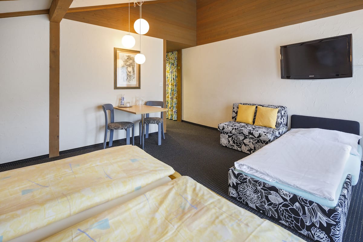 A hotel room with two beds, a sofa, a table with chairs, a television, and a framed picture on the wall.