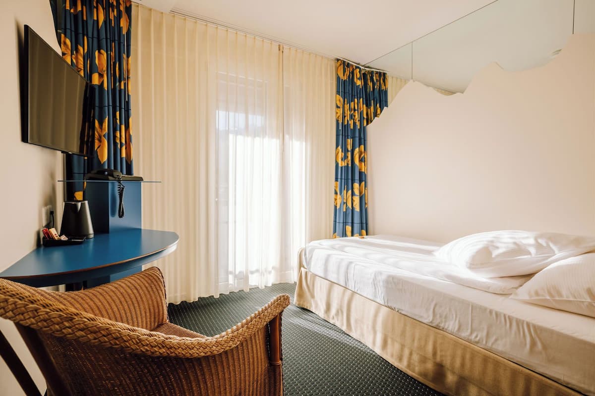 A hotel room with a bed, a desk with a chair, a television, and curtains.