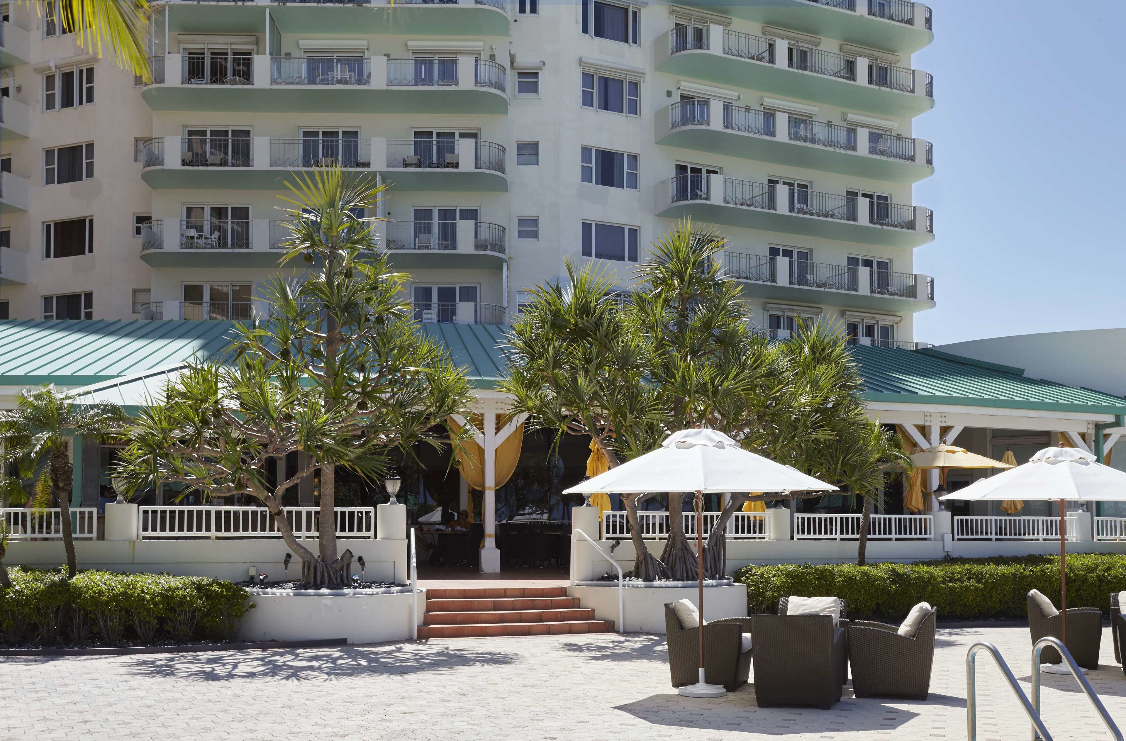 Un hôtel à plusieurs étages doté de balcons, d’un espace extérieur aménagé avec des sièges et d’une zone couverte avec des parasols.
