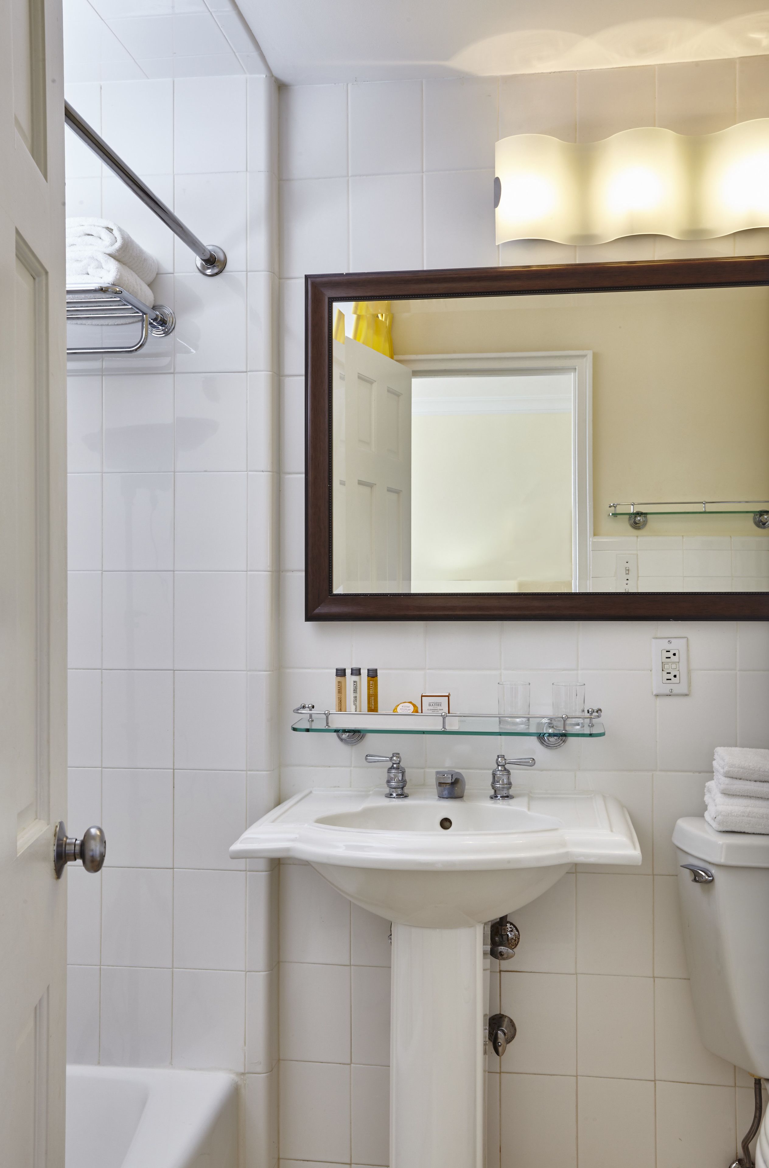 A bathroom with a white sink, a mirror, and a glass shelf with toiletries.