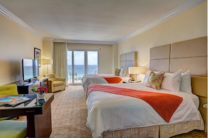 A hotel room with two beds, a desk with a computer, a chair, and a view of the sea.
