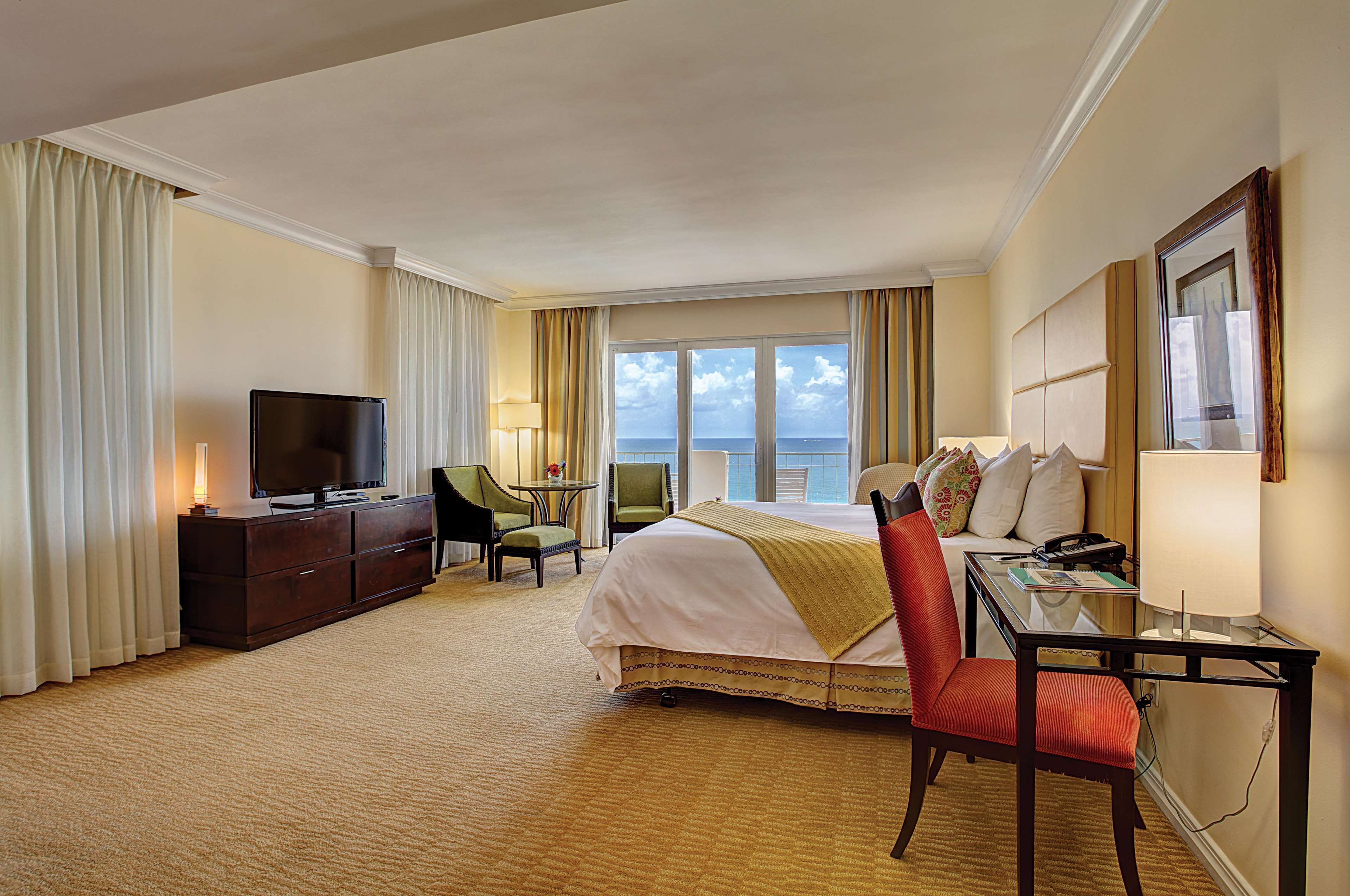 Ein Hotelzimmer mit Bett, Schreibtisch, Stuhl, Fernseher und Meerblick.