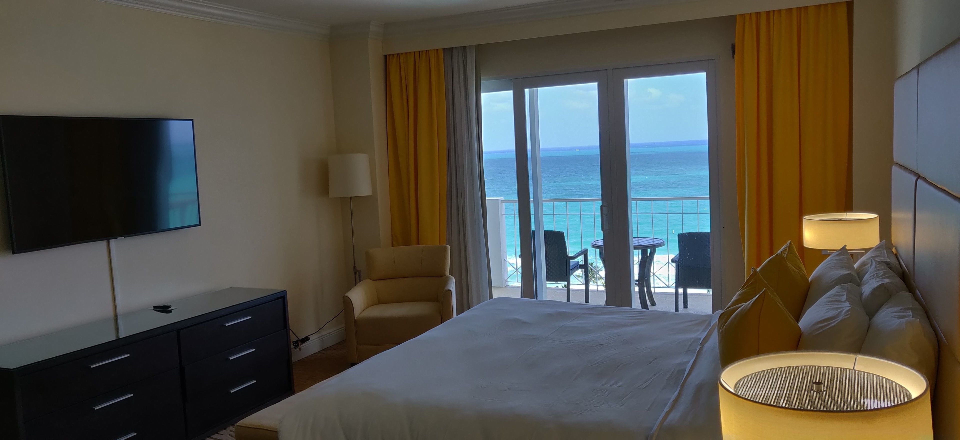 Ein Hotelzimmer mit einem großen Bett, einem Fernseher, einem Schreibtisch und Meerblick durch die Balkontüren.