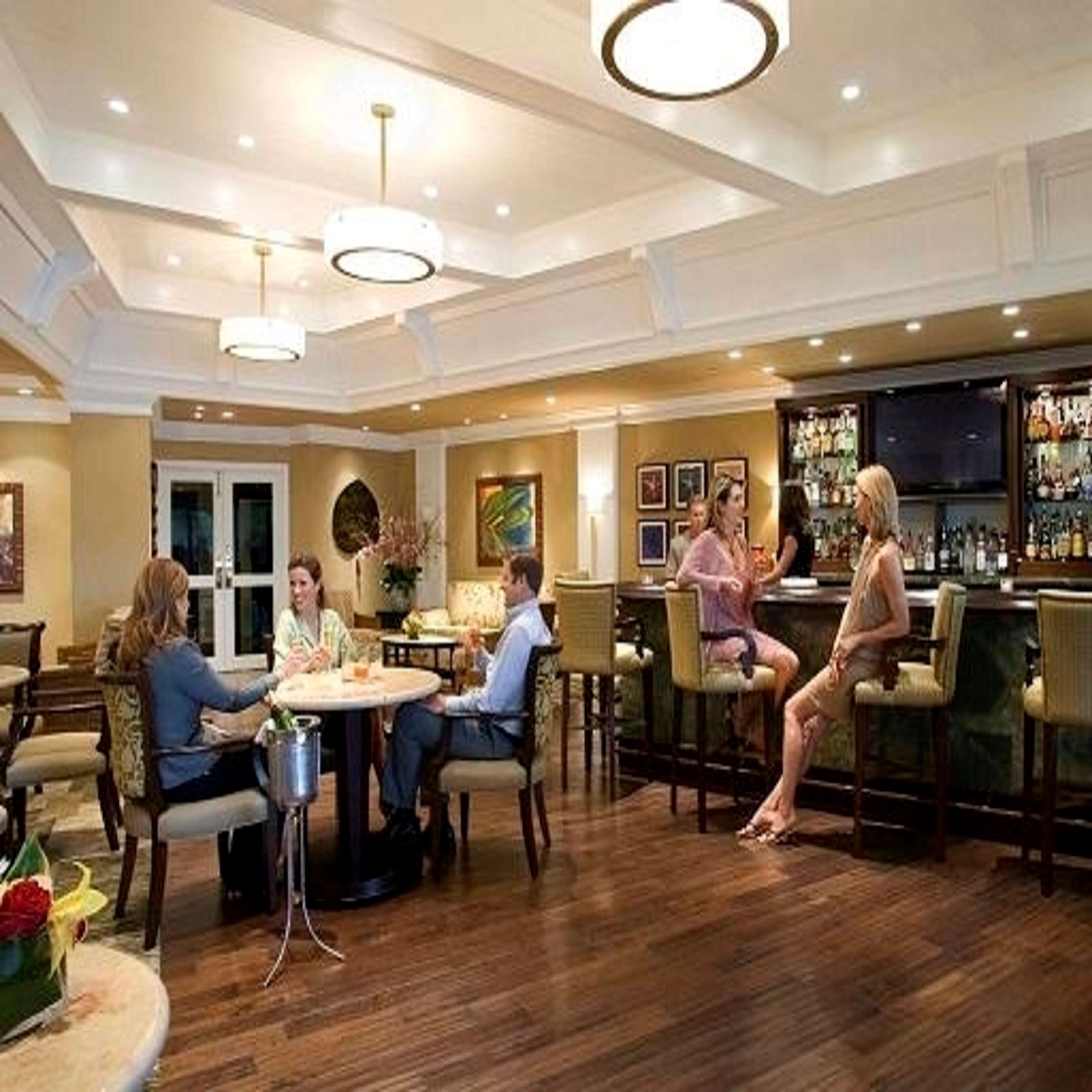A bar area with a counter and seating. There are people seated at a table with a drink.