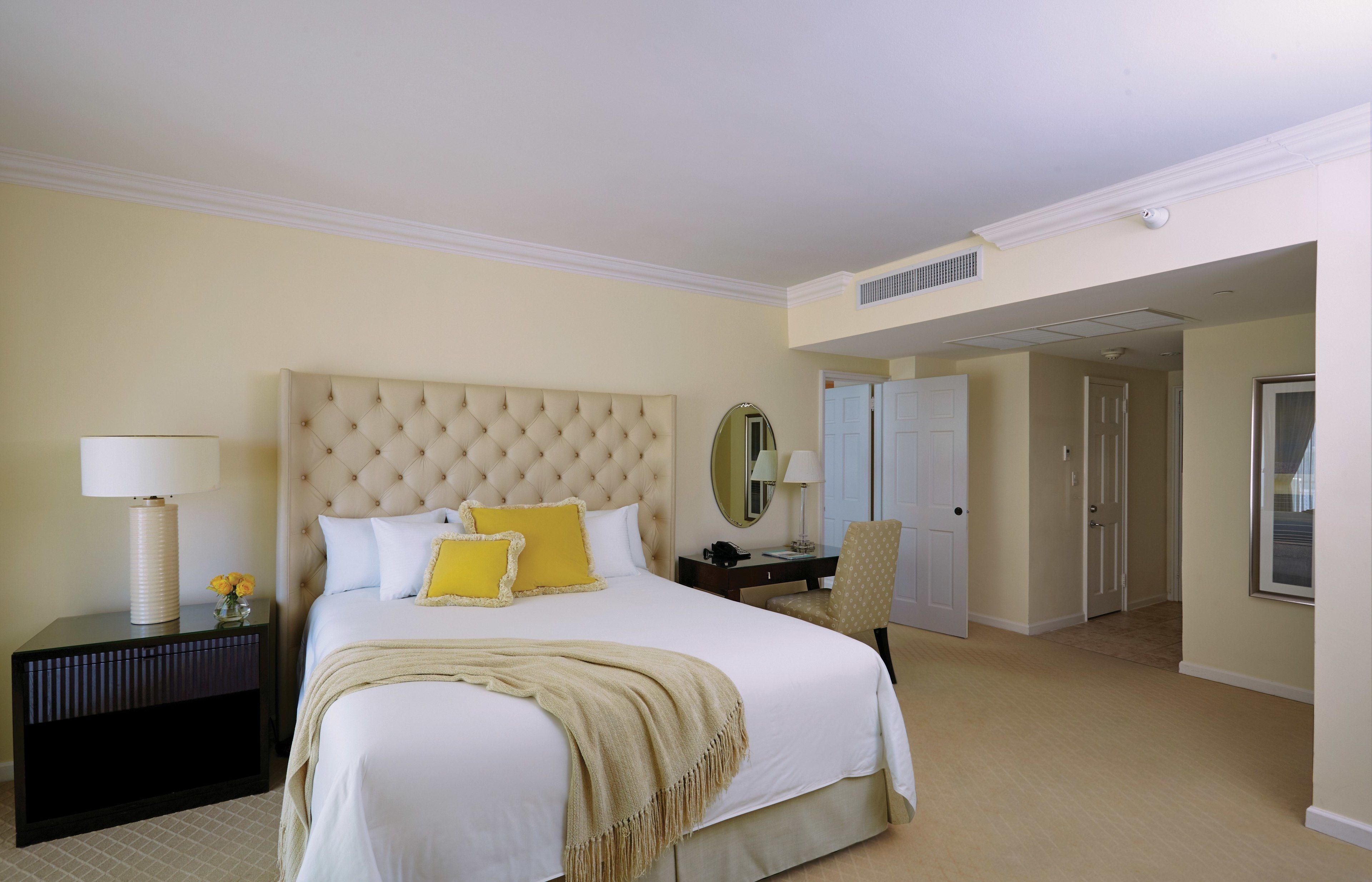 A hotel bedroom with a large bed, a nightstand, a chair, a desk, and a mirror.