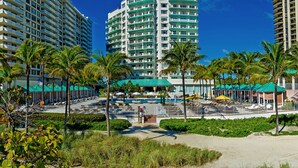 A high-rise hotel with multiple balconies, a pool area with umbrellas, and palm trees. - Sea View Hotel, Bal Harbour, On The Ocean (Bal Harbour)